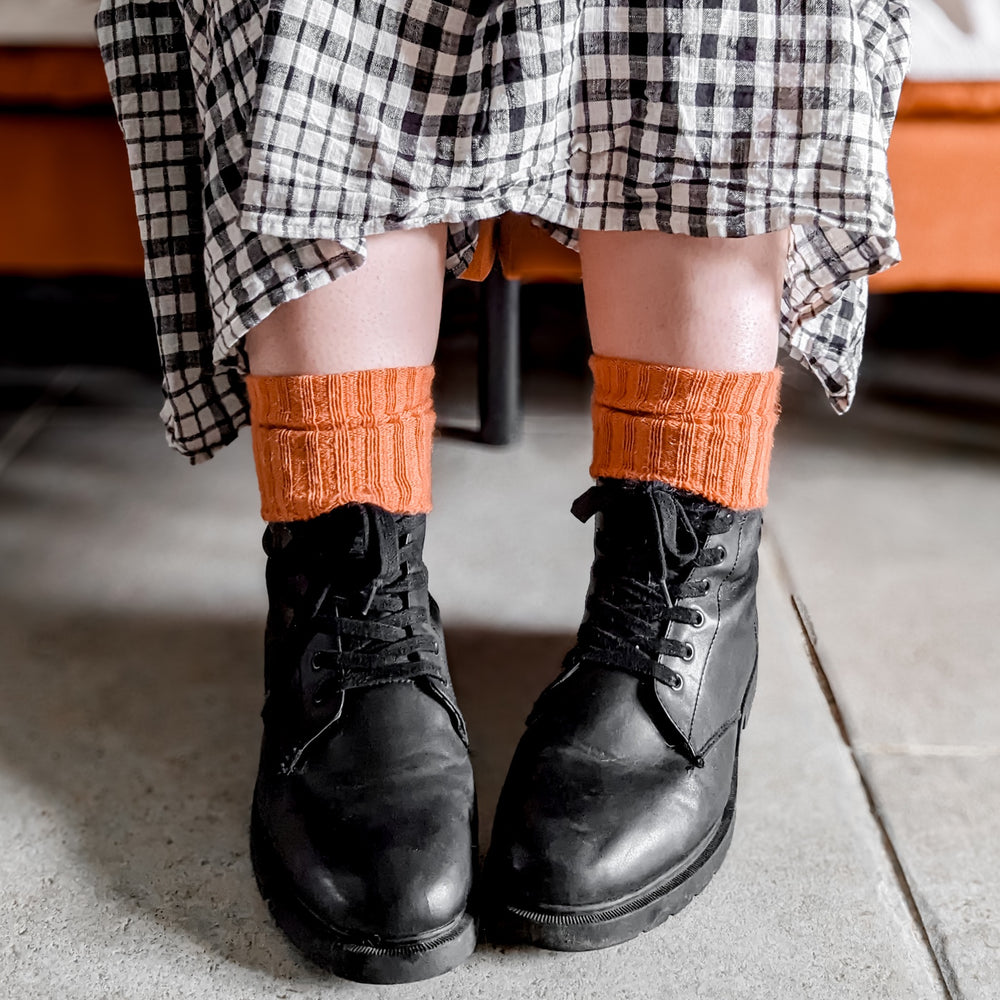 
                      
                        Burnt orange Sussex-style Capricorn Mohair Socks with textured knit, styled with boots and a checked dress – bold, cosy everyday socks with flair
                      
                    